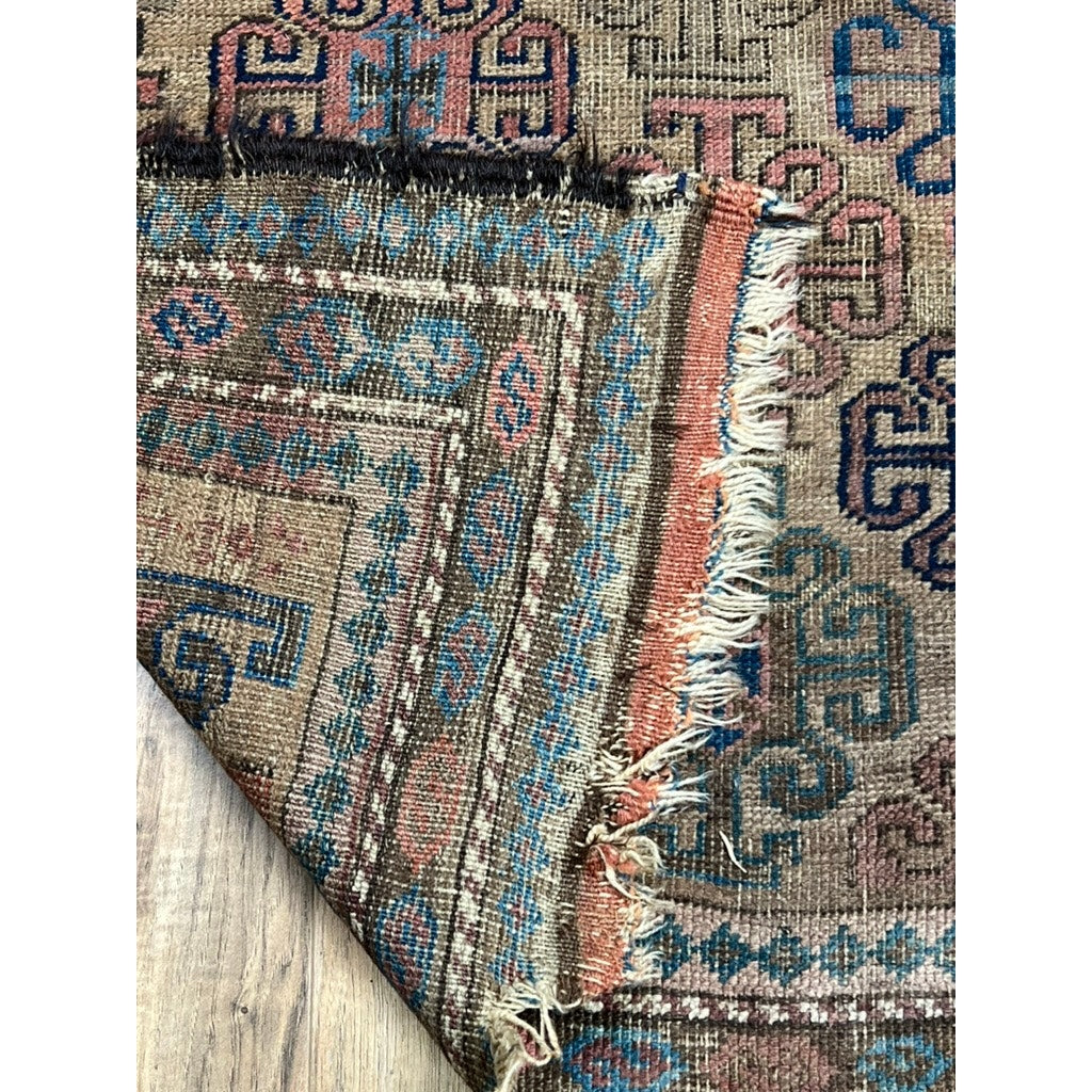 A close-up of an Antique Baluch Rug with Tree of Life variant motif, Northeast Persia, mid-19th c. (3’x5’), shows its folded corner revealing front and back sides, geometric designs in blue, brown, red, and visible fraying.