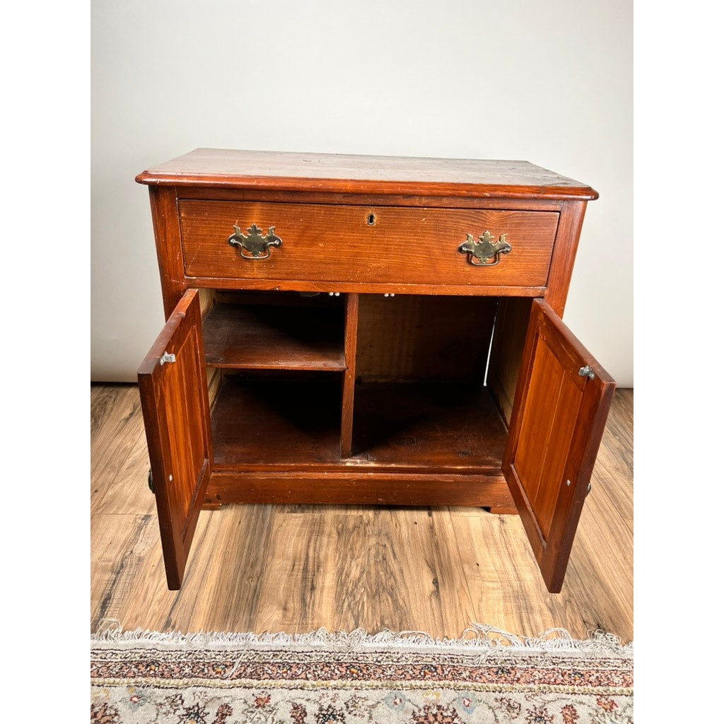 The Antique Victorian Pine Commode c. 1900 features a single drawer, two open doors revealing four compartments, and stands on wooden flooring with a patterned rug partially visible below.