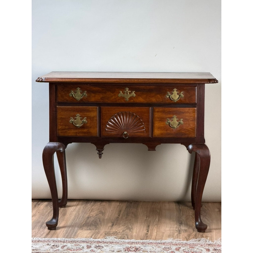 18th Century American Queen Anne Walnut Shell-Carved Lowboy, c. 1740–1770, featuring three drawers with ornate brass handles, a shell-carved center drawer, and elegantly curved legs in classic 18th-century style. This antique walnut piece is shown standing on a wood floor with part of a rug visible beneath. Brand: None/Unknown.