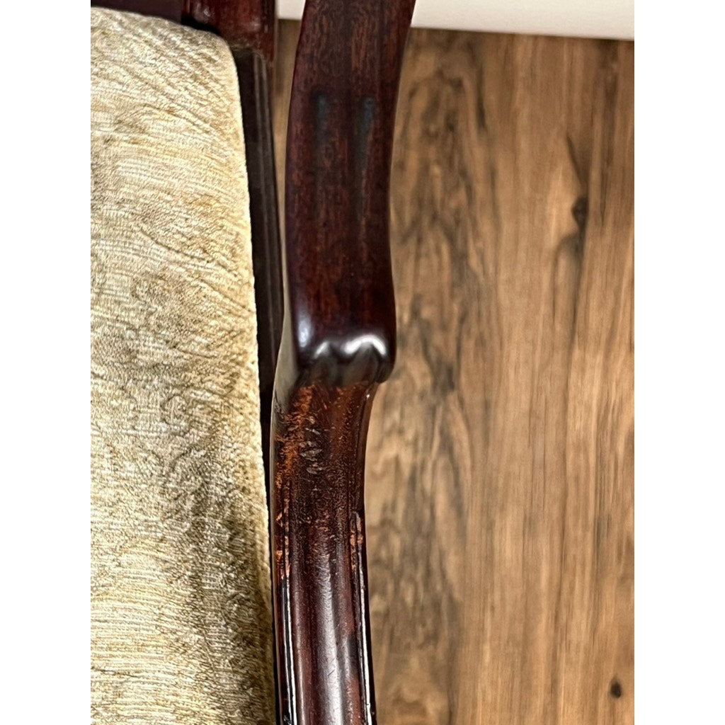 Close-up of an Antique English George III Mahogany Hepplewhite Armchair (early 19th century), showing its scratched wood arm and beige upholstered seat, highlighting period craftsmanship on a wooden floor.