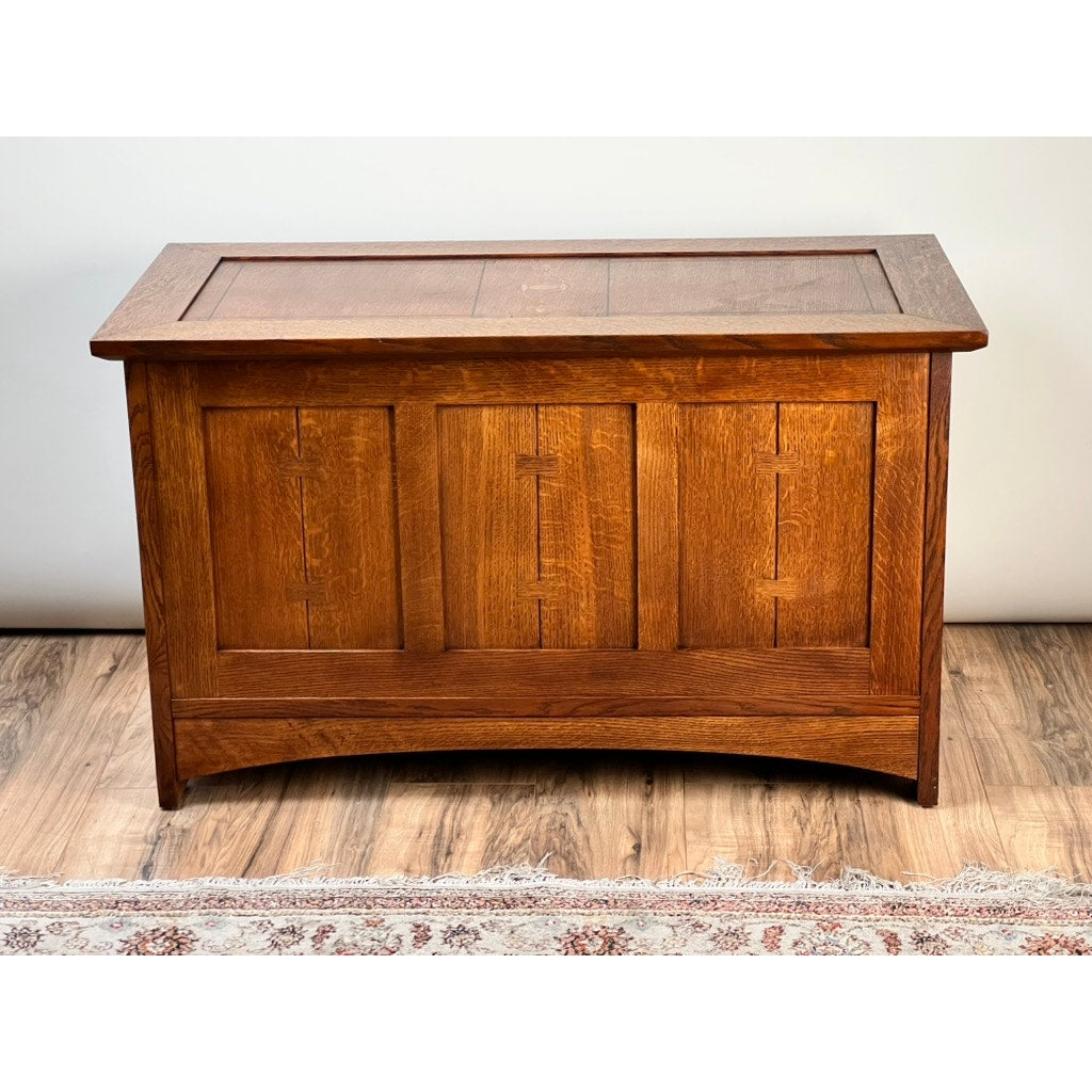 The Vintage Stickley Harvey Ellis Millennium Edition Oak Blanket Chest by Stickley features a rectangular form, paneled sides, flat lid, and warm medium-brown finish in the Arts & Crafts style, set on hardwood flooring with a patterned rug in view.