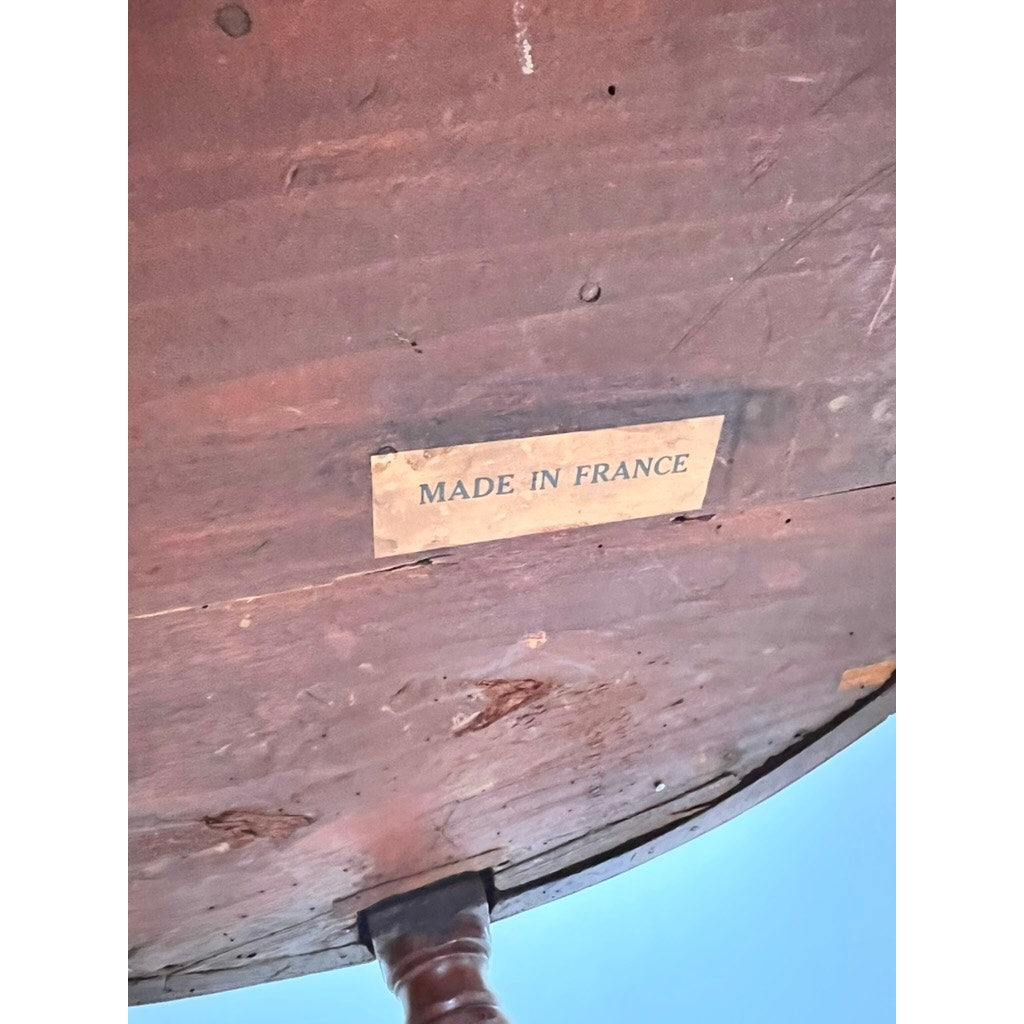 A close-up of the underside of an Antique 19th Century French Louis XVI-Style Mahogany Bouillotte Table with Marble Top shows a rectangular label reading MADE IN FRANCE. Brand is unknown.