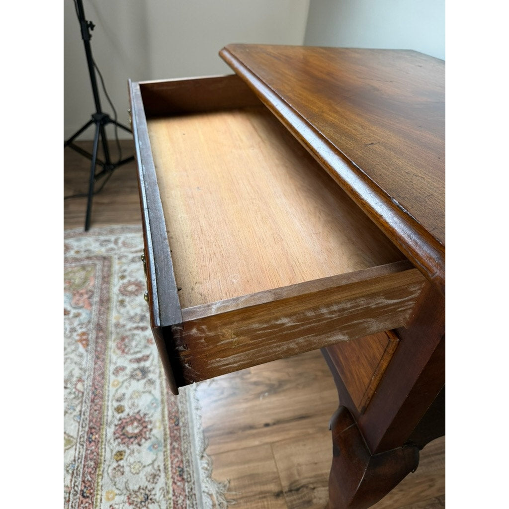 An open drawer in an 18th Century American Queen Anne Walnut Shell-Carved Lowboy (c. 1740–1770) reveals an empty interior. The antique table sits on a wooden floor beside a patterned rug, with a tripod visible in the background.
