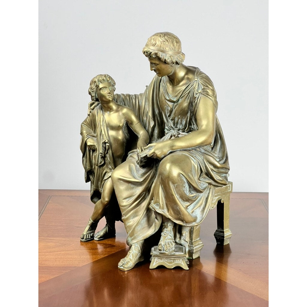 Antique Bronze Sculpture “Teacher and Pupil” by Louis Charles Janson, 1865, signed Ch. Janson—features a seated woman in classical attire with a young boy beside her, both on a wooden surface against a plain background.