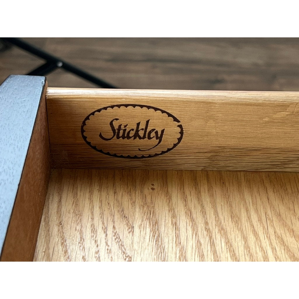 A close-up of a Vintage Federal Style Edge Banded Mahogany End Table by Stickley shows the "Stickley" logo burned inside an oval on the drawer edge, with a wood floor in the background.