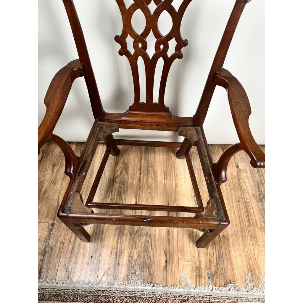 An Antique Chippendale Walnut Open Arm Chair (c. late 18th century), lacking its seat cushion and showing the open frame, stands on a wooden floor beside the edge of a patterned rug. Brand: None/Unknown.