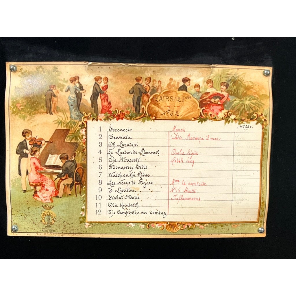 An Antique Swiss 12 Tune Music Box from the late 19th century features a cream backdrop, floral border, and handwritten French notes listing classical pieces, evoking Victorian charm and gatherings around music. Brand Unknown.