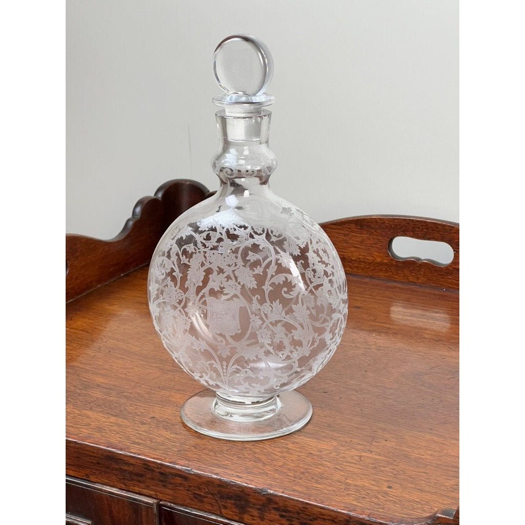 A Vintage Baccarat Crystal Decanter in the "Michelangelo" pattern for Martell Cognac c. 1930, featuring ornate etching and a round stopper, rests on a polished wooden tray with cutout handles.