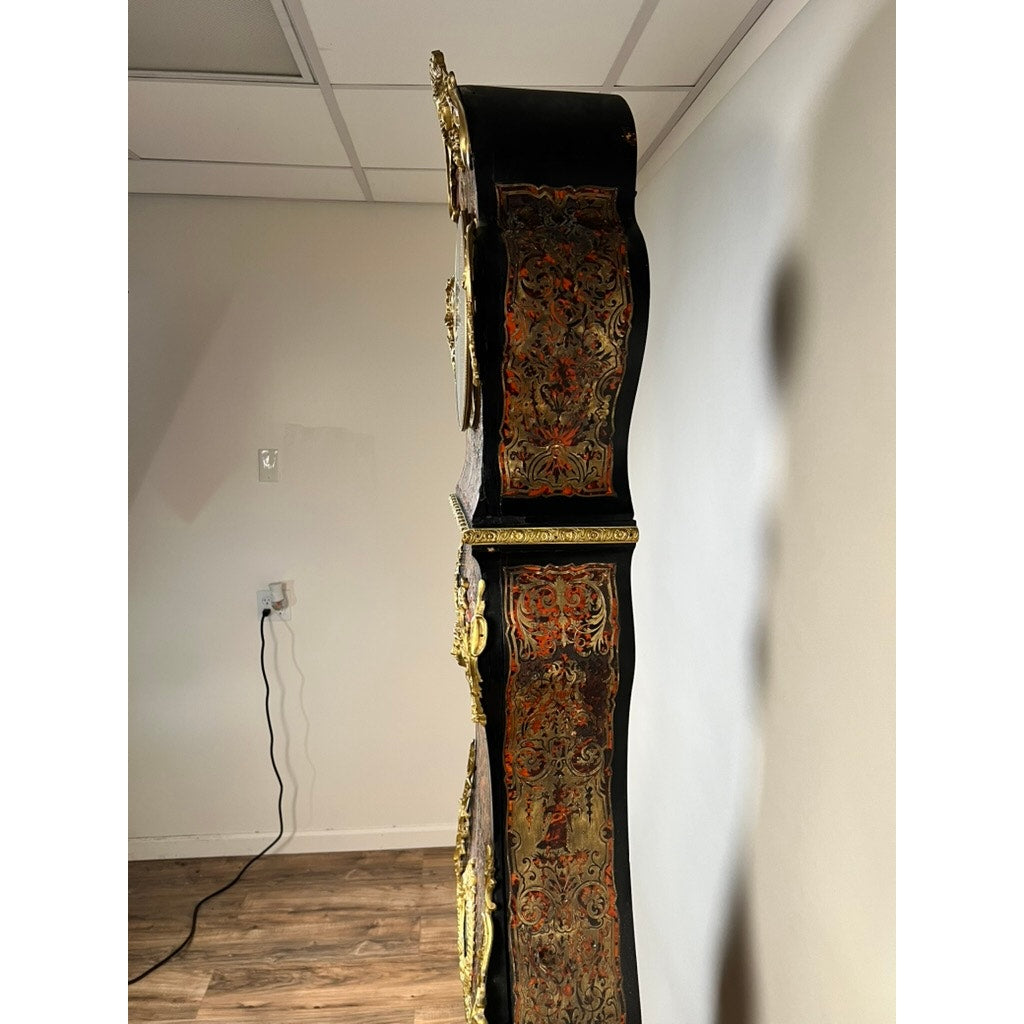 Side view of a Monumental French Napoleon III Boulle Marquetry Floor Clock with Ormolu Mounts, circa 1865–1885, featuring ornate gold detailing and exquisite marquetry work. The clock stands against a plain wall in a room with wood flooring, while an electrical outlet and cord in the background subtly contrast with its display of French decorative artistry.