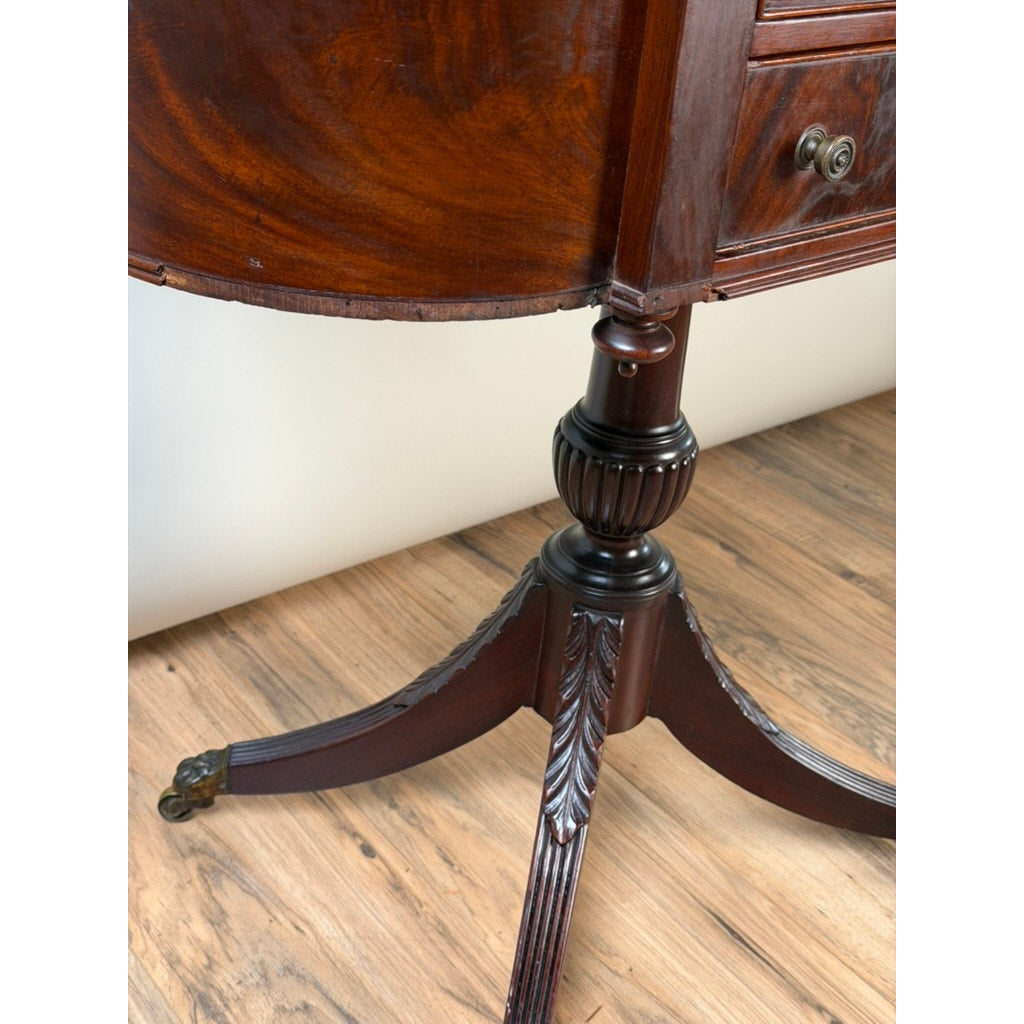 Close-up of the carved leg of an Early 19th Century New York Classical Mahogany Astragal-End Work Table in the manner of Duncan Phyfe, c. 1815–1825, featuring detailed woodwork and a brass caster wheel on a wooden floor. The table’s rich, dark finish and partially visible drawer exemplify the refined craftsmanship characteristic of mahogany furniture from this era. Brand: None or Unknown.