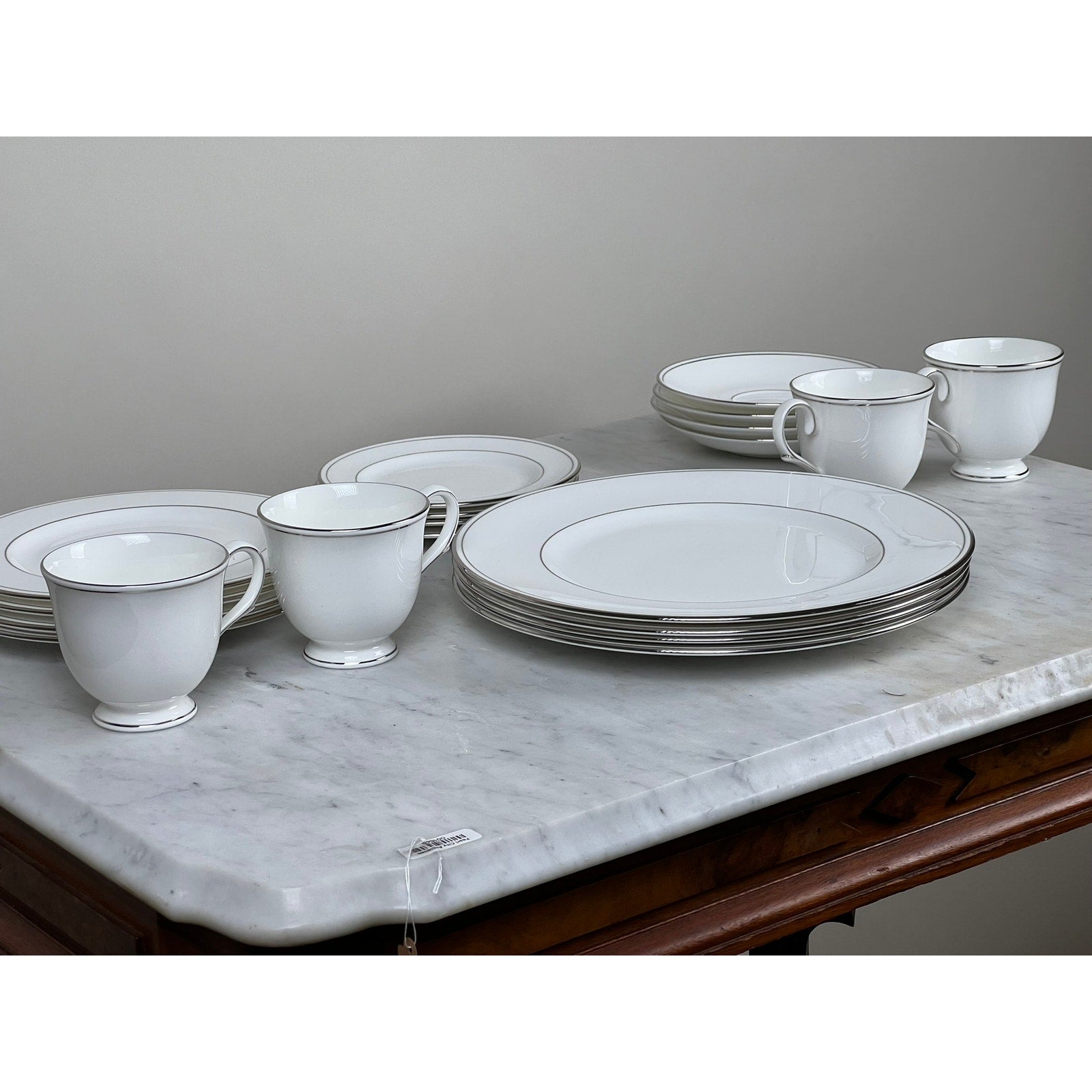 A Vintage Lenox Federal Platinum Fine English Bone China Service for Four, with plates, bowls, and cups featuring silver trim, is neatly arranged on a marble-topped wooden table.