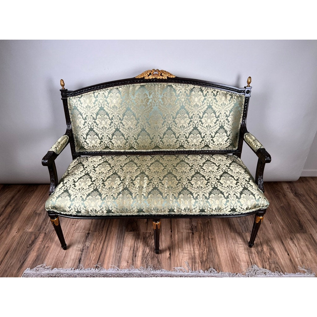 Vintage Louis XVI Style Settee in green damask upholstery features ornate carvings, a dark frame with gold accents, and rests partly on a light rug over wood flooring. Brand: None/Unknown.