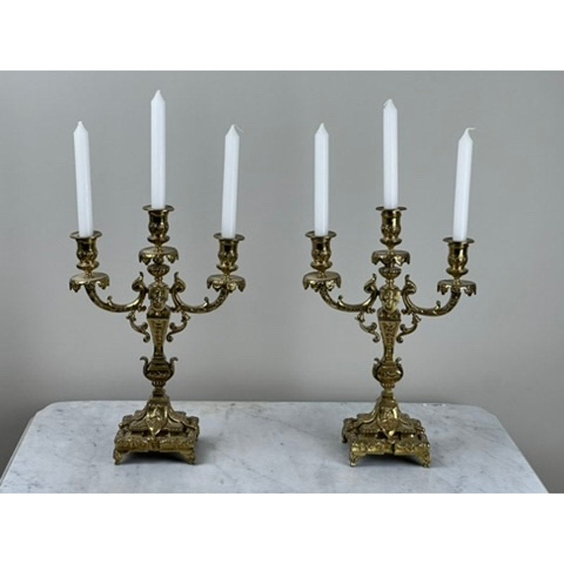 An Antique Pair of Late 19th Century Brass Three Light Candelabra, each with white taper candles, are displayed on a white marble surface against a gray background—a striking addition to Victorian home decor.