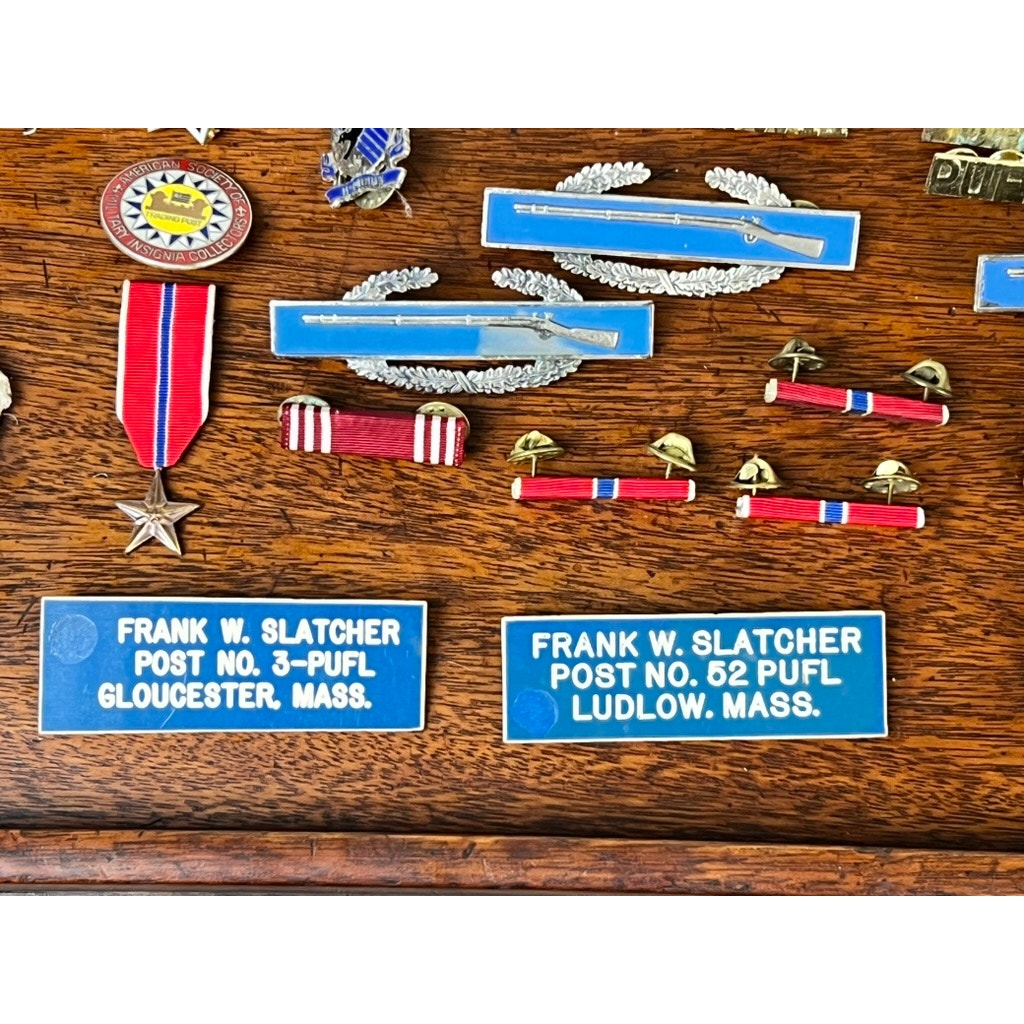 A display of the Attributed WWII 158th Infantry Bushmasters Grouping of Frank W. Slatcher, Company I, Pacific Theater, with medals, ribbons, blue nameplates, and memorabilia honoring his service.