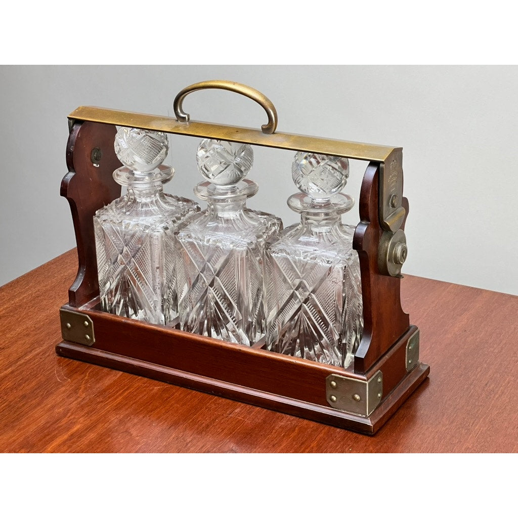 The Antique English Edwardian Betjemann’s Cut Crystal Three Bottle Tantalus c. Early 20th Century features three intricately cut crystal decanters with stoppers, set in a brass-handled wooden frame by Betjemann's.