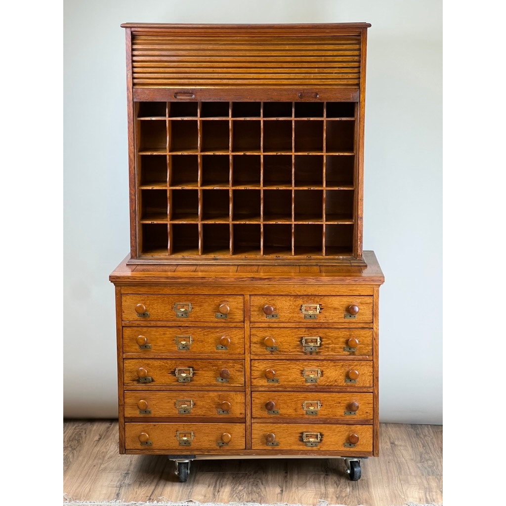 An Antique Early 20th Century Oak Multidrawer File with Roll Top Pigeon Hole Top features small lower drawers, open cubbies above, a partially open tambour door revealing square slots, and rests on wheels. Brand unknown.