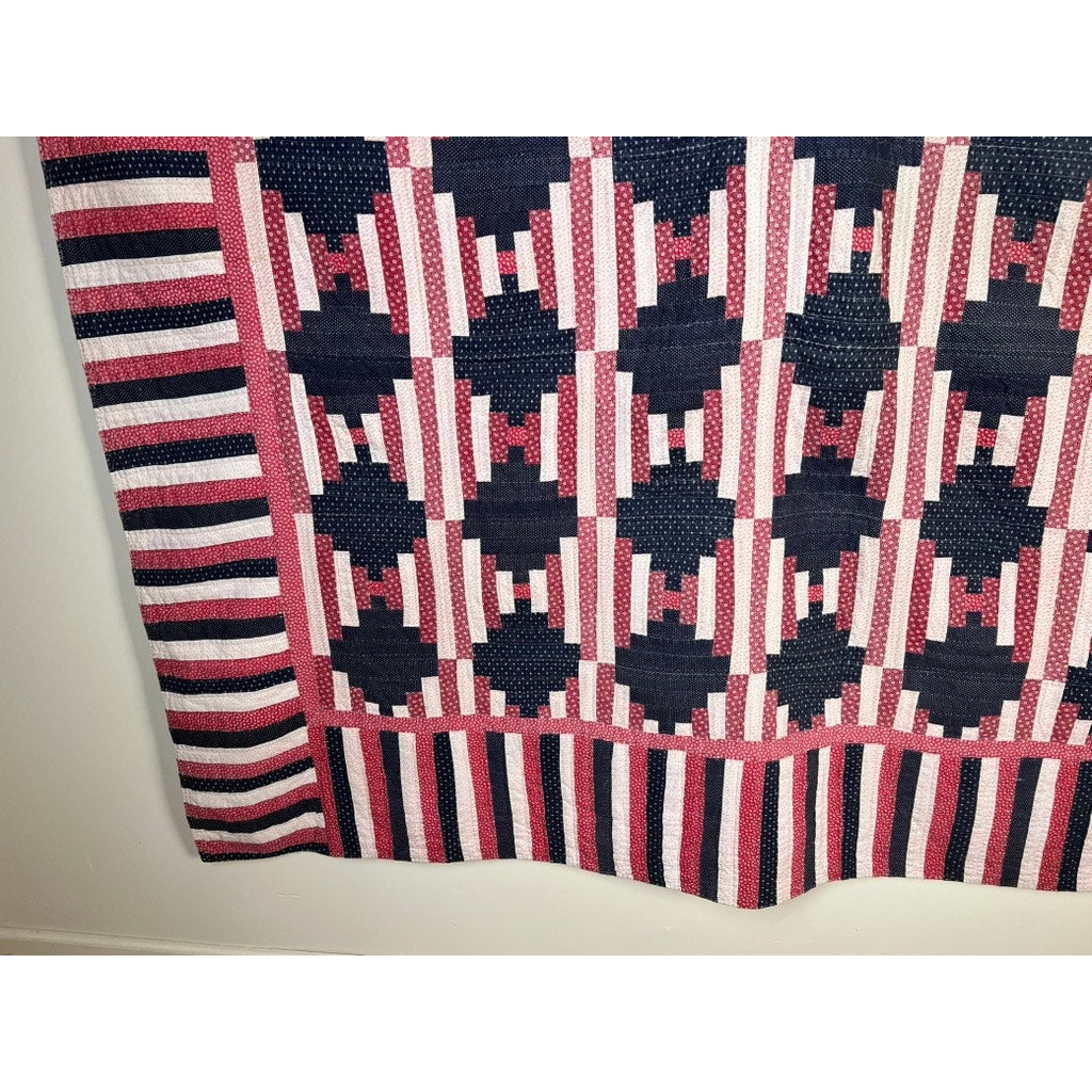A matching pair of antique American patriotic hand-quilted Log Cabin quilts (early 20th century) with geometric square and diamond patterns and striped borders hangs against a light wall, echoing classic Americana charm.