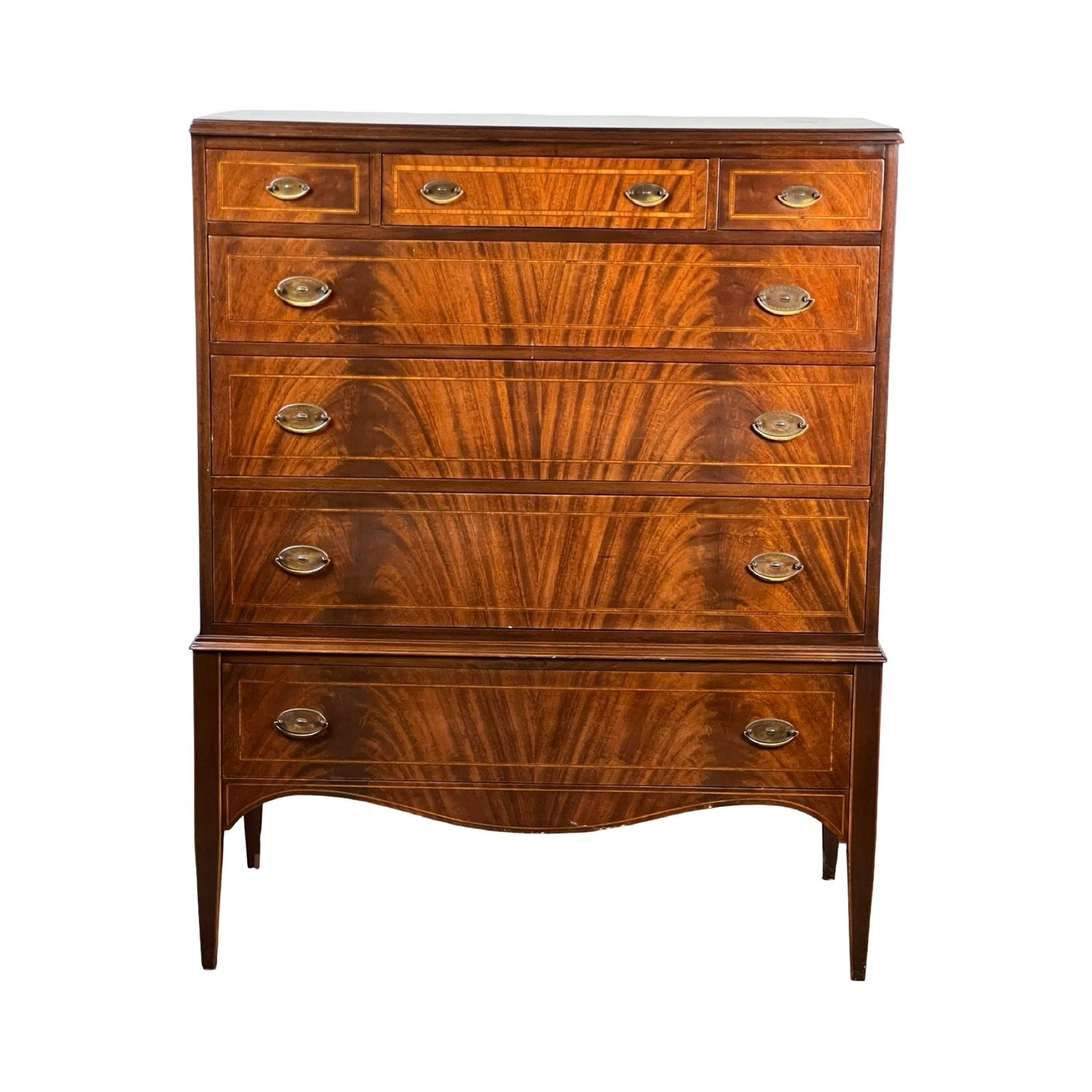 A vintage Dutch Woodcraft Shops Federal Style Flame Mahogany Chest on Stand, crafted circa 1945–1955, featuring six drawers with brass handles, elegant flame mahogany grain patterns, and classic tapered legs with curved details that showcase the timeless craftsmanship of Dutch Woodcraft Shops.