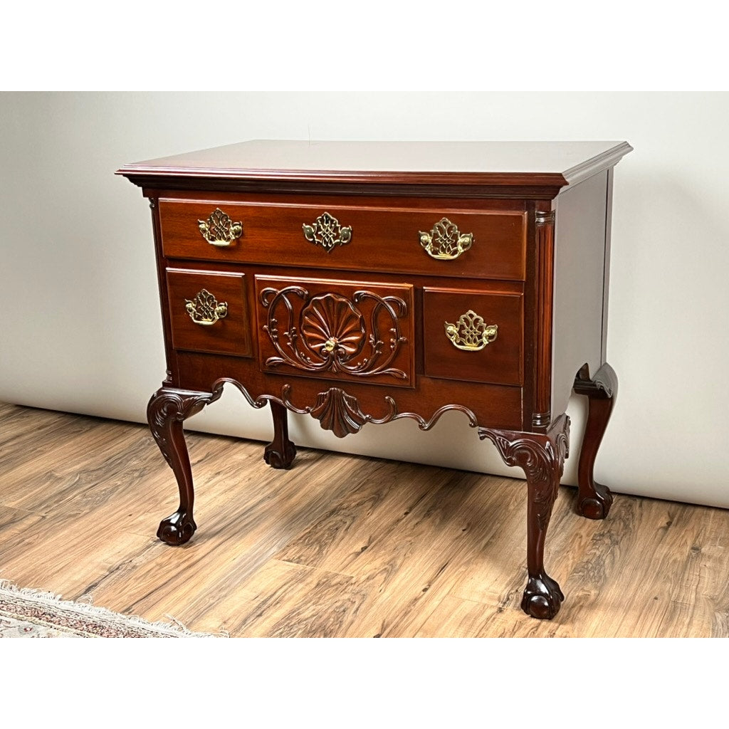The Vintage Solid Mahogany Chippendale Style Lowboy by Councill Craftsmen features ornate brass handles, intricate front carvings, and curved legs. It stands on a wood floor against a plain light wall.