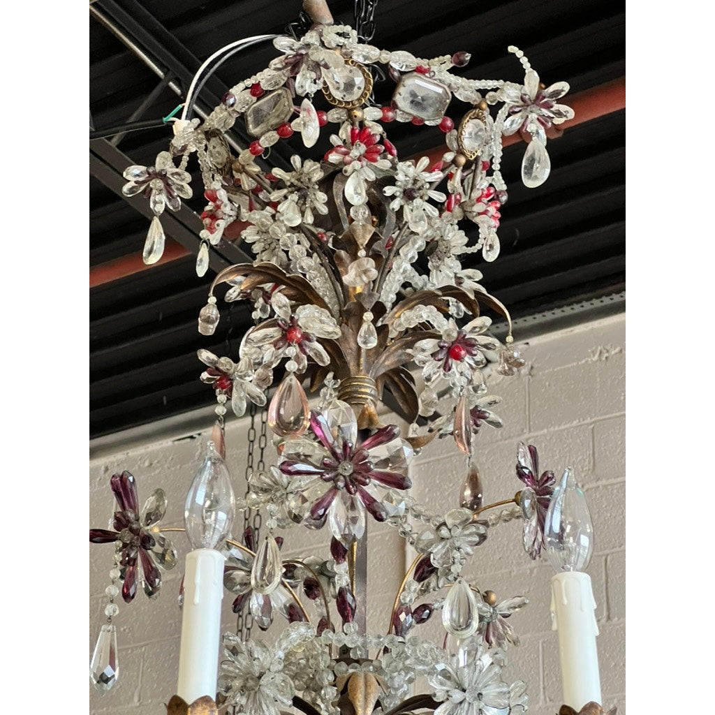 A close-up of an Antique Late 19th Century French Rococo Tole Amethyst and Crystal Ten Light Chandelier, featuring amethyst and clear crystals, set against a light brick wall with a black ceiling and exposed pipes.