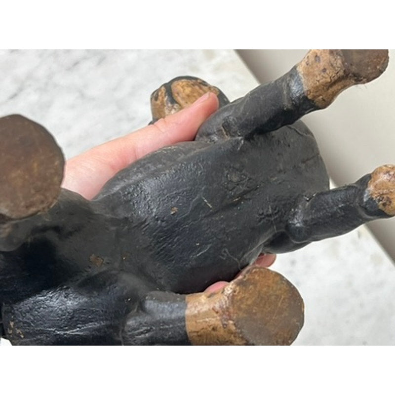 A hand holds an Antique Cast Iron Boston Terrier Doorstop by Hubley upside down, displaying its underside and worn brown-painted feet against a light, speckled background.