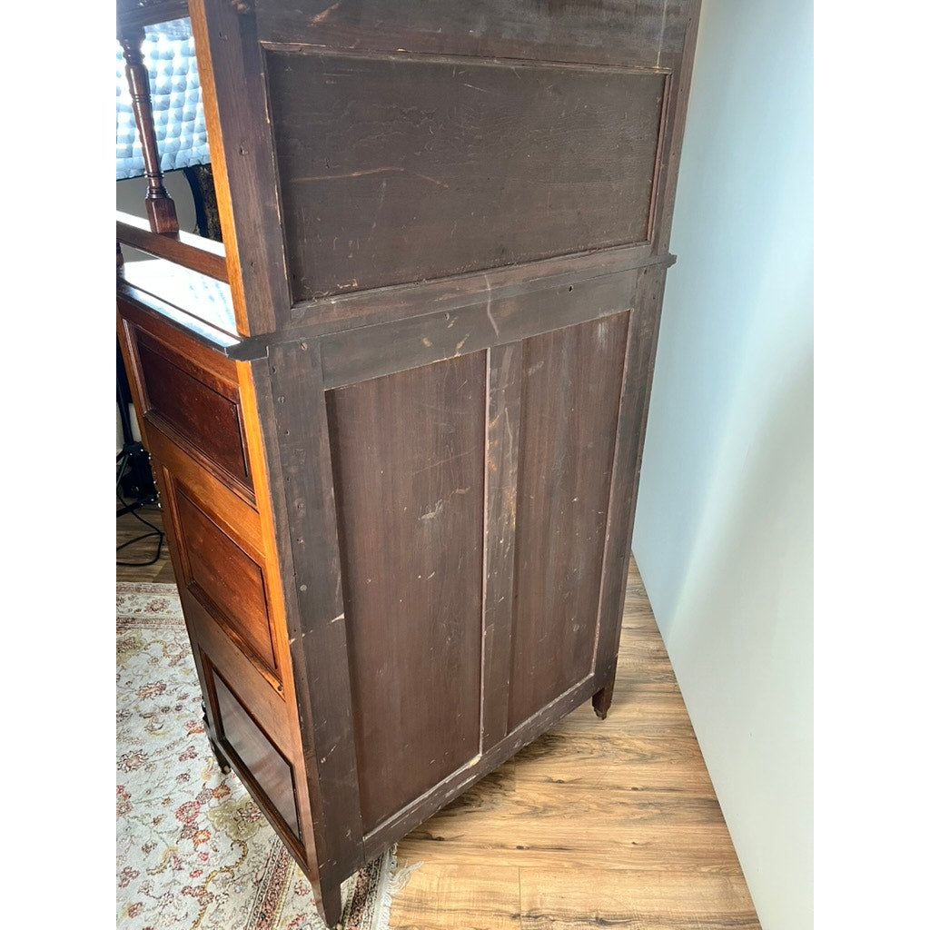 The Antique Victorian Aesthetic Movement Mahogany Four Over Four Gentlemen’s Chest c. 1880 is shown from the back and side, displaying a dark, slightly worn panel. It rests on a wooden floor next to a decorative rug with some drawers visible on the left.