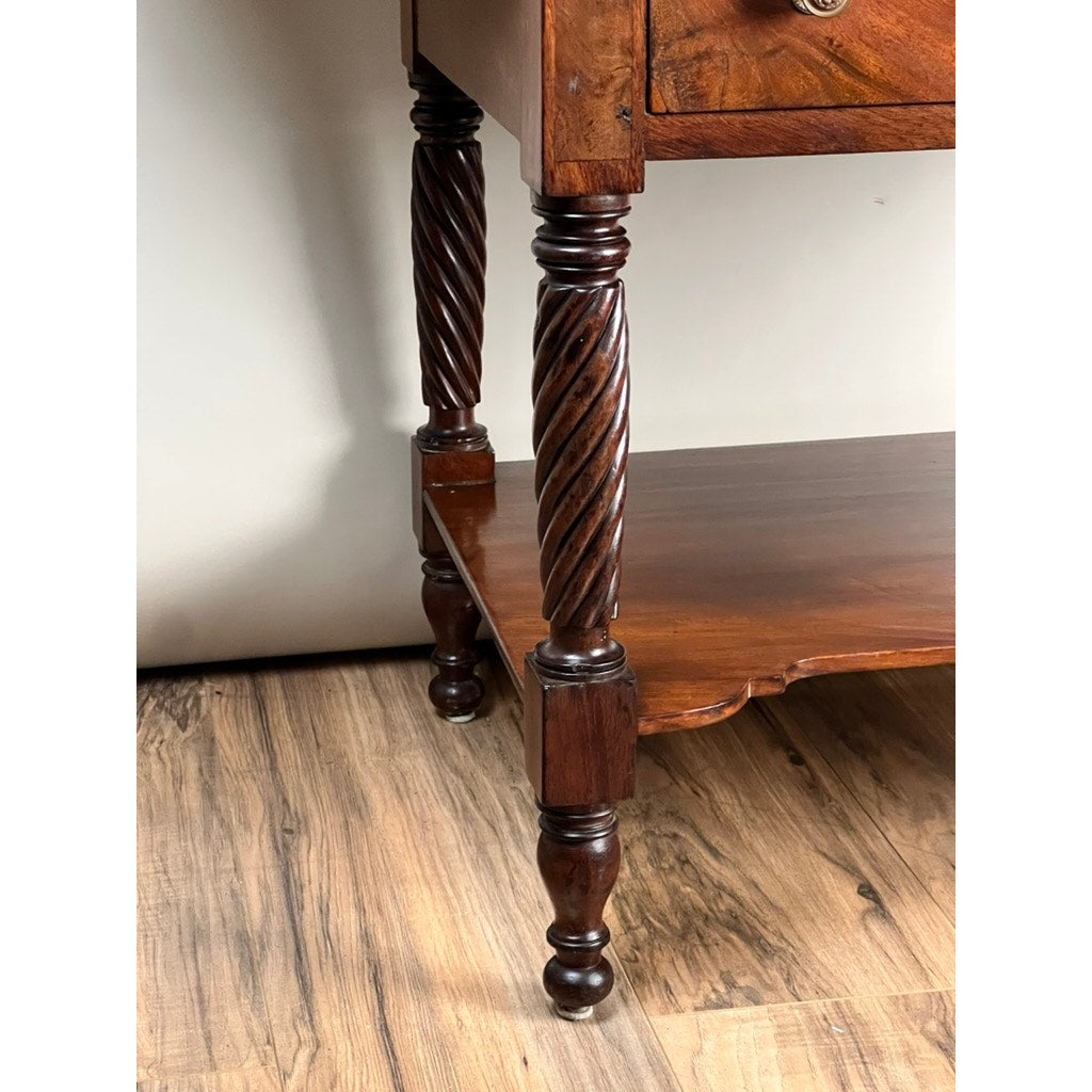 Close-up of an Antique Federal Mahogany Two Drawer Work Stand c. 1820 with lions head pulls, spiral-carved legs, and a lower shelf. This elegant piece stands on a wood-patterned floor against a light-colored wall.