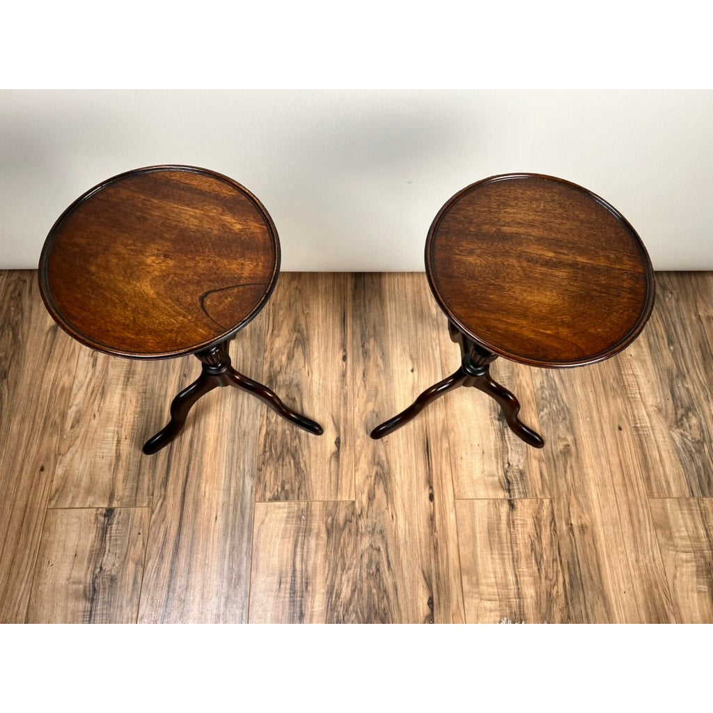 A pair of Vintage Match Pair Diminutive Walnut Candle Stands c. 1940, each with a dark polished top and three curved legs, stand on a wood-patterned floor against a plain light-colored wall.