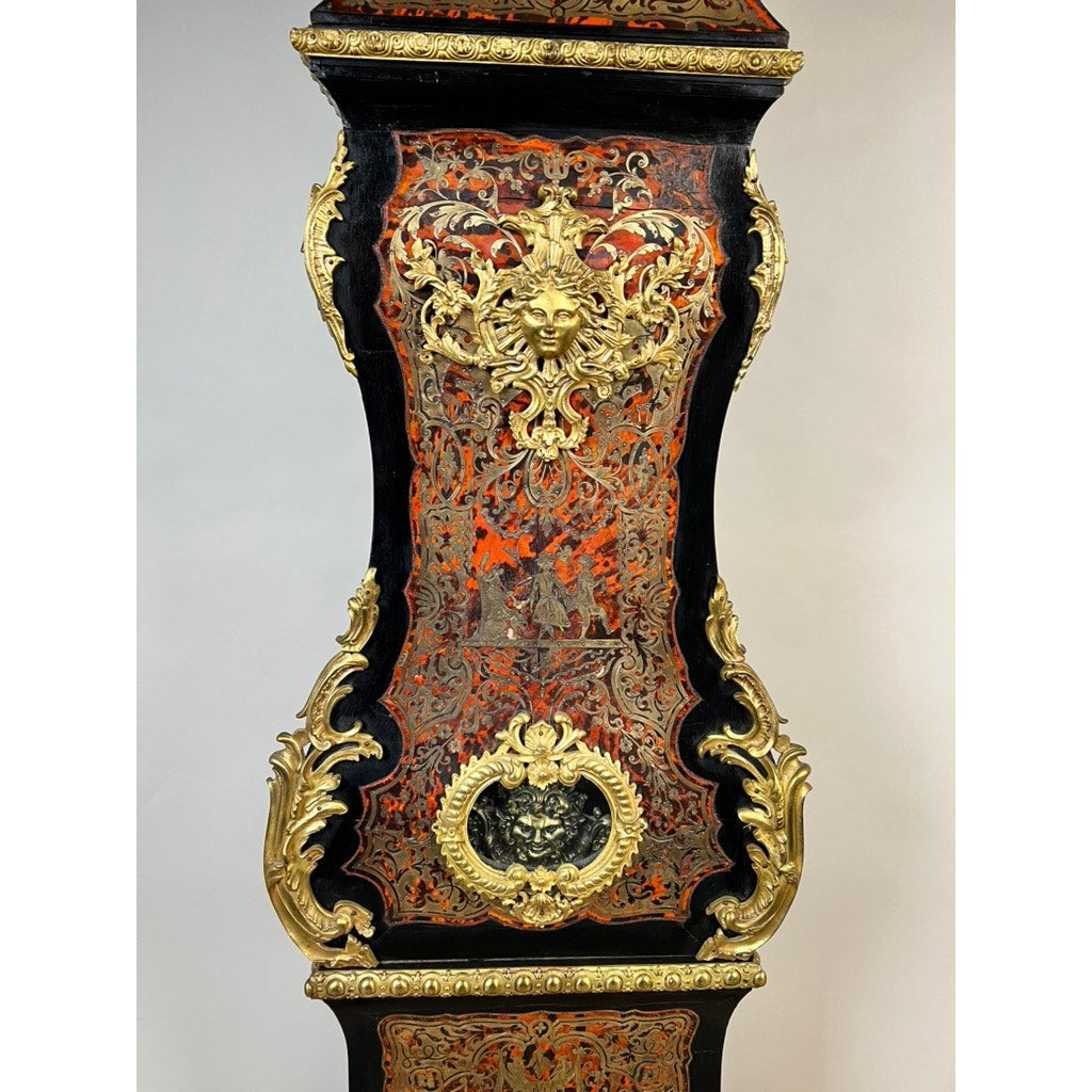 Introducing the Monumental French Napoleon III Boulle Marquetry Floor Clock with Ormolu Mounts, Circa 1865–1885: This impressive floor clock boasts an ornate case adorned with intricate gold detailing, rich red patterns, and a gilt face featuring flowing hair at its center. Surrounded by elaborate scrollwork and decorative motifs on a striking black background, the piece exemplifies masterful Boulle marquetry and reflects the sophisticated elegance of French decorative artistry from the late 19th century.