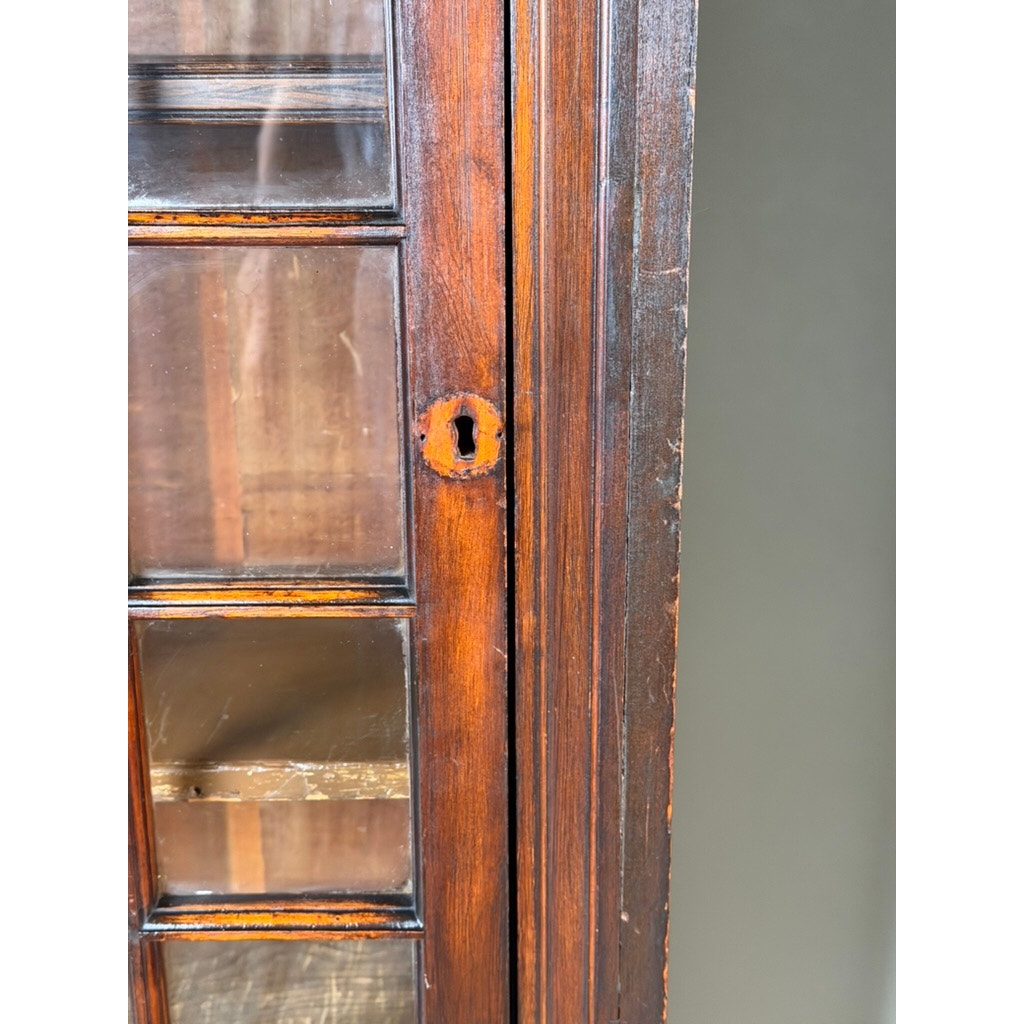 Close-up of a Pair of Mid-19th Century New England Cherry Glazed Display Cupboards by Pearl City Antiques, c. 1840–1860. The image highlights an aged, oval keyhole with visible wear and scratches on the cherry wood door, while interior shelves can be seen through the original glass panels, evoking the craftsmanship of early American cupboards.