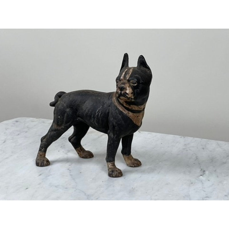 An antique cast iron Boston Terrier doorstop, probably Hubley, features a black and brown dog with pointed ears standing alert—prized by collectors and displayed on a white marble surface against a light background.