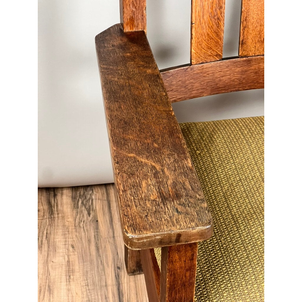 Close-up of an Antique Quarter Sawn Mission Oak Arm Chair by Quaint Furniture c. 1920, showing the wooden armrest, vertical slats on the back, green textured seat cushion, and wood floor—classic Arts & Crafts style.