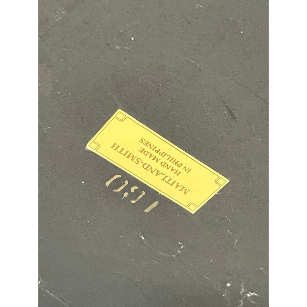 A yellow label on a dark surface reads "MAITLAND SMITH HAND MADE IN PHILIPPINES" (upside down), with faint numbers 1680 below—likely from a vintage Maitland-Smith Leather-Clad Occasional Table.