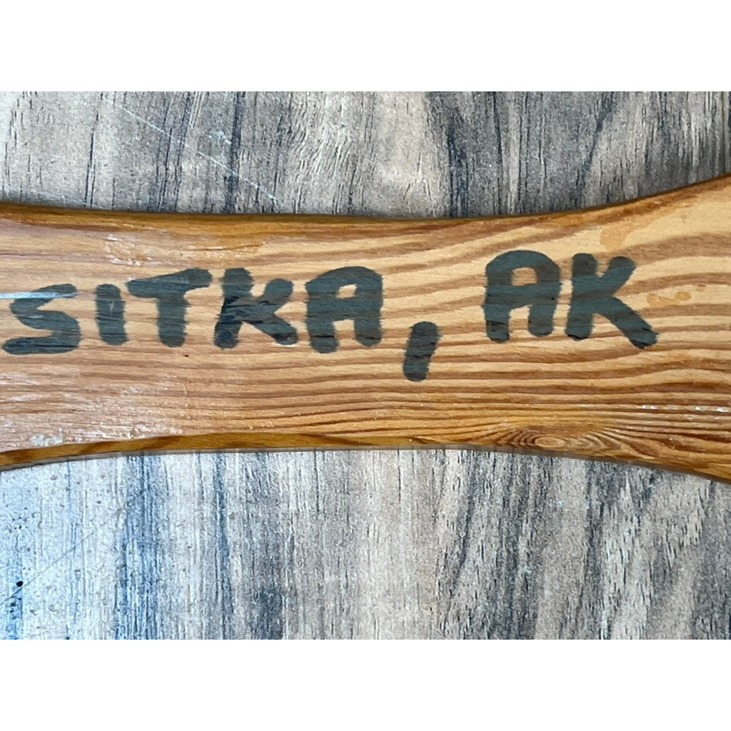 A close-up of a Vintage Inuit Carved Red Cedar Paddle from Sitka, Alaska, signed illegibly. The visible wood grain highlights its craftsmanship against a textured gray background, showcasing Indigenous Alaska art.