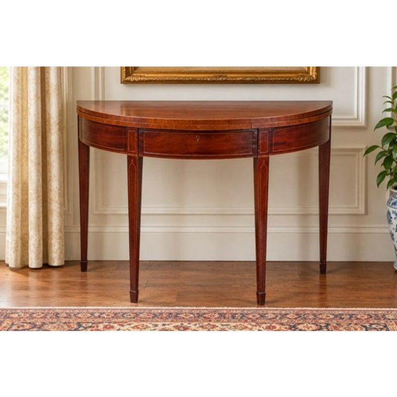 An English George III Mahogany and Satinwood-Inlaid Demilune Games Table, circa 1790–1810, featuring a semicircular top, four tapered legs, and light wood inlay.