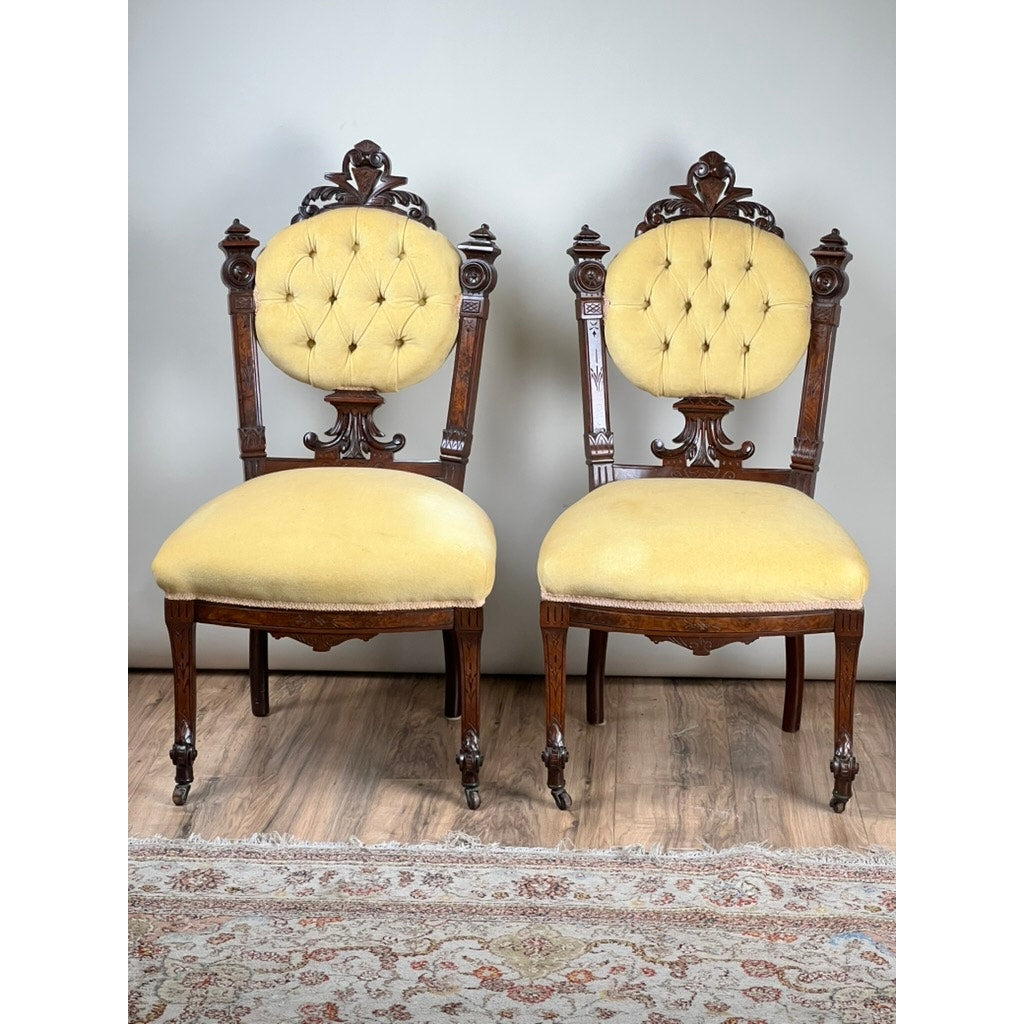 A fine antique pair of Renaissance Revival walnut side chairs, attributed to John Jelliff (Newark, c. 1880), feature carved dark wood frames and round tufted yellow backs and seats, displayed side by side on a wooden floor with a rug in front.