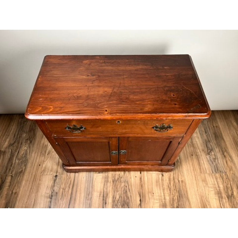 The Antique Victorian Pine Commode c. 1900 features a polished brown finish, two drawers with metal handles, and two doors below—ideal for bedroom storage. It stands on a wood floor against a light-colored wall. Brand: None/Unknown.