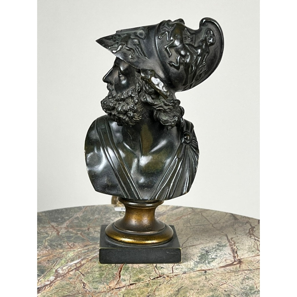 Antique Small Bronze Bust of King Menelaus, late 19th century, featuring a detailed crested helmet with Greek mythological figures. Displayed on a pedestal atop a marbled surface, the bust depicts Menelaus looking to the left. Brand unknown.