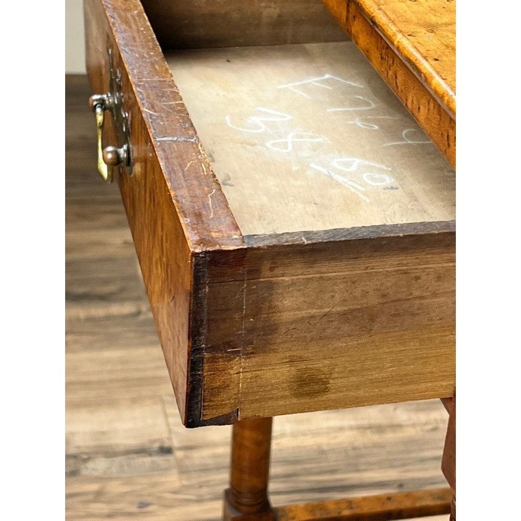 An Antique Sheraton Birdseye Maple One Drawer Stand from the early 19th century, with visible wear, a brass handle, and chalk markings inside the open drawer, reflects classic American furniture style on a wooden floor. Brand: Unknown.