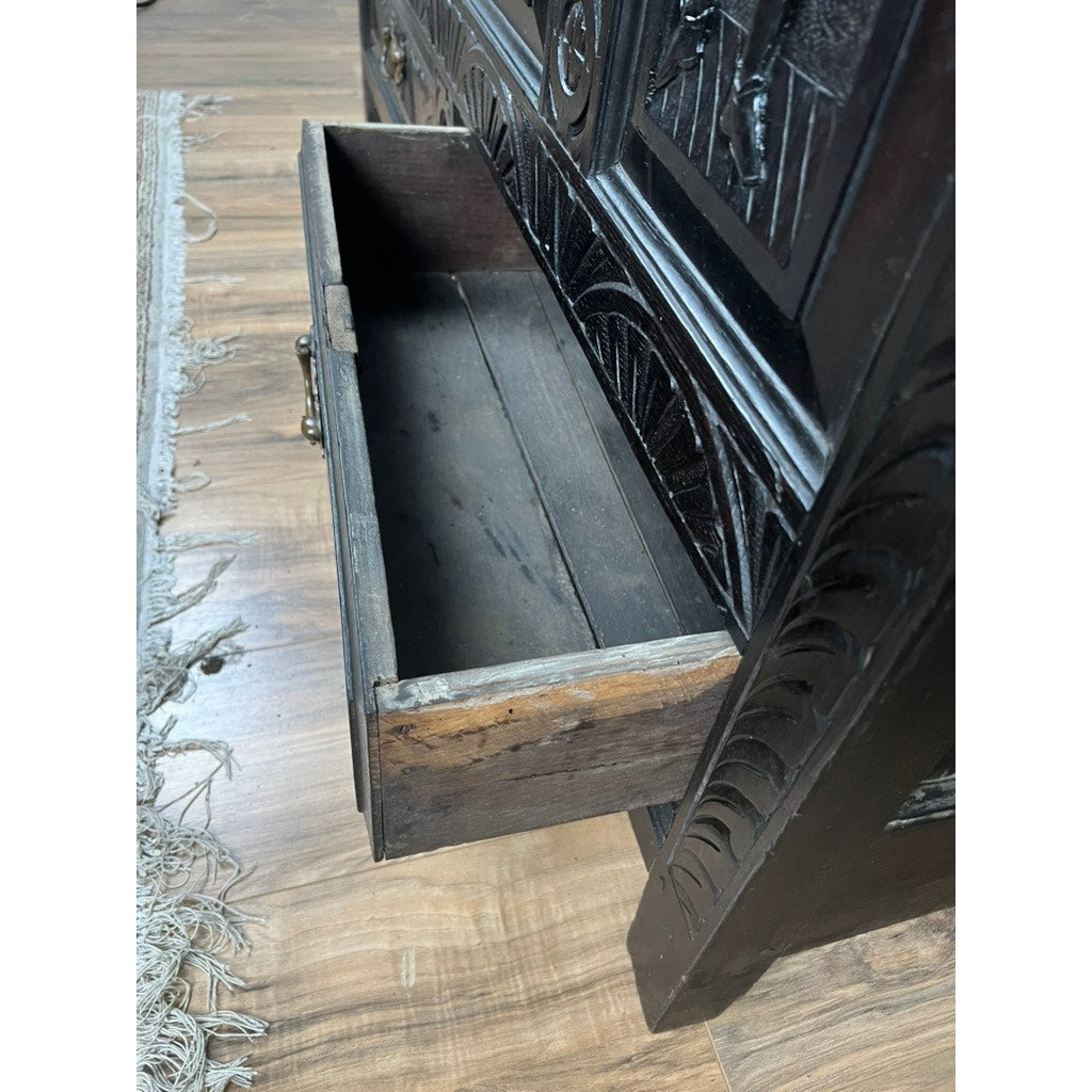 A close-up of an open, empty, ornately carved drawer in an Antique 18th Century Charles II Style Mule Chest, possibly Irish or Scottish, placed on a wooden floor with part of a fringed rug visible to the left.