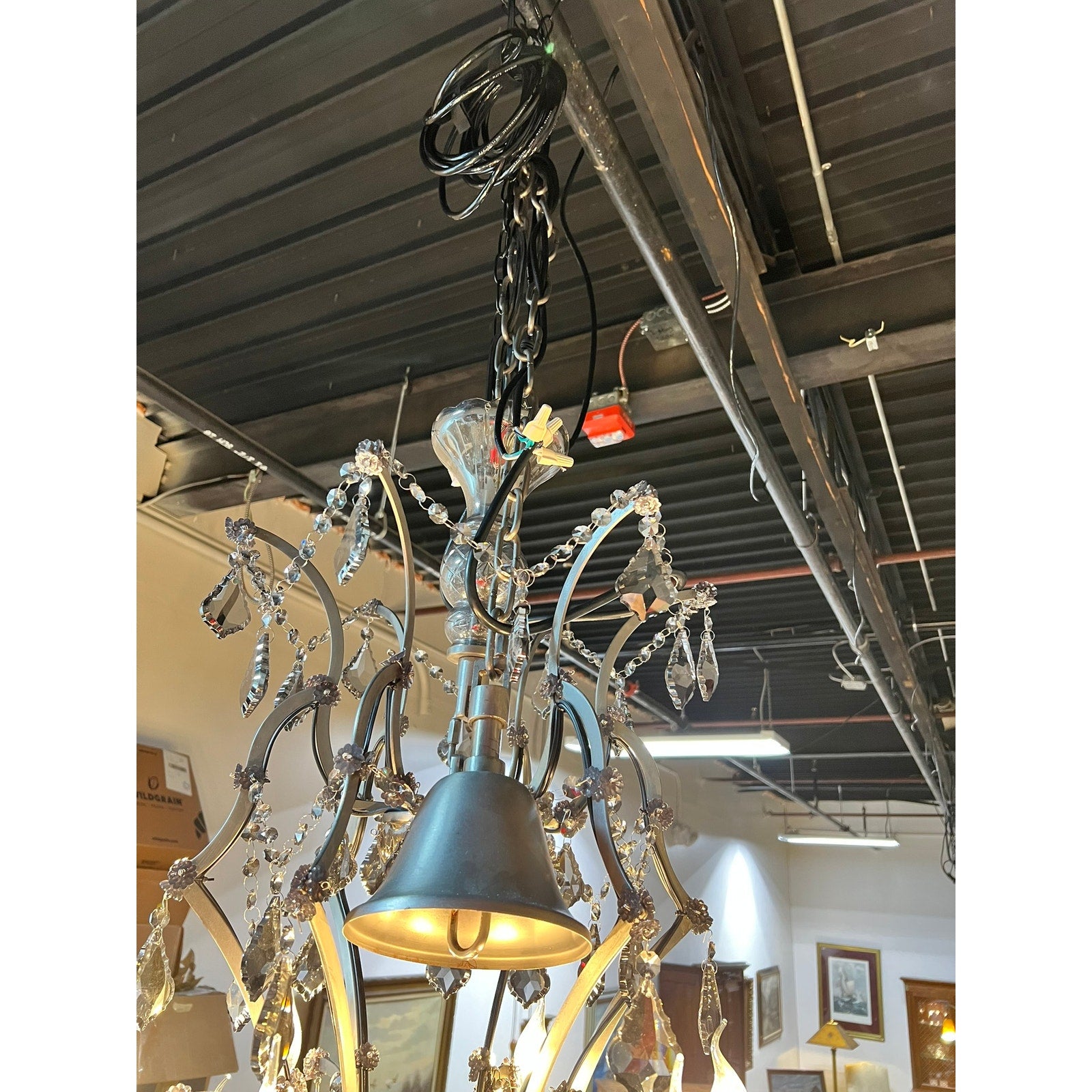 The Large Vintage Smoke Crystal 24 Light Chandelier hangs from black cords and chains in a room with industrial-style exposed pipes, its tiered smoke crystal accents adding elegance to the space.