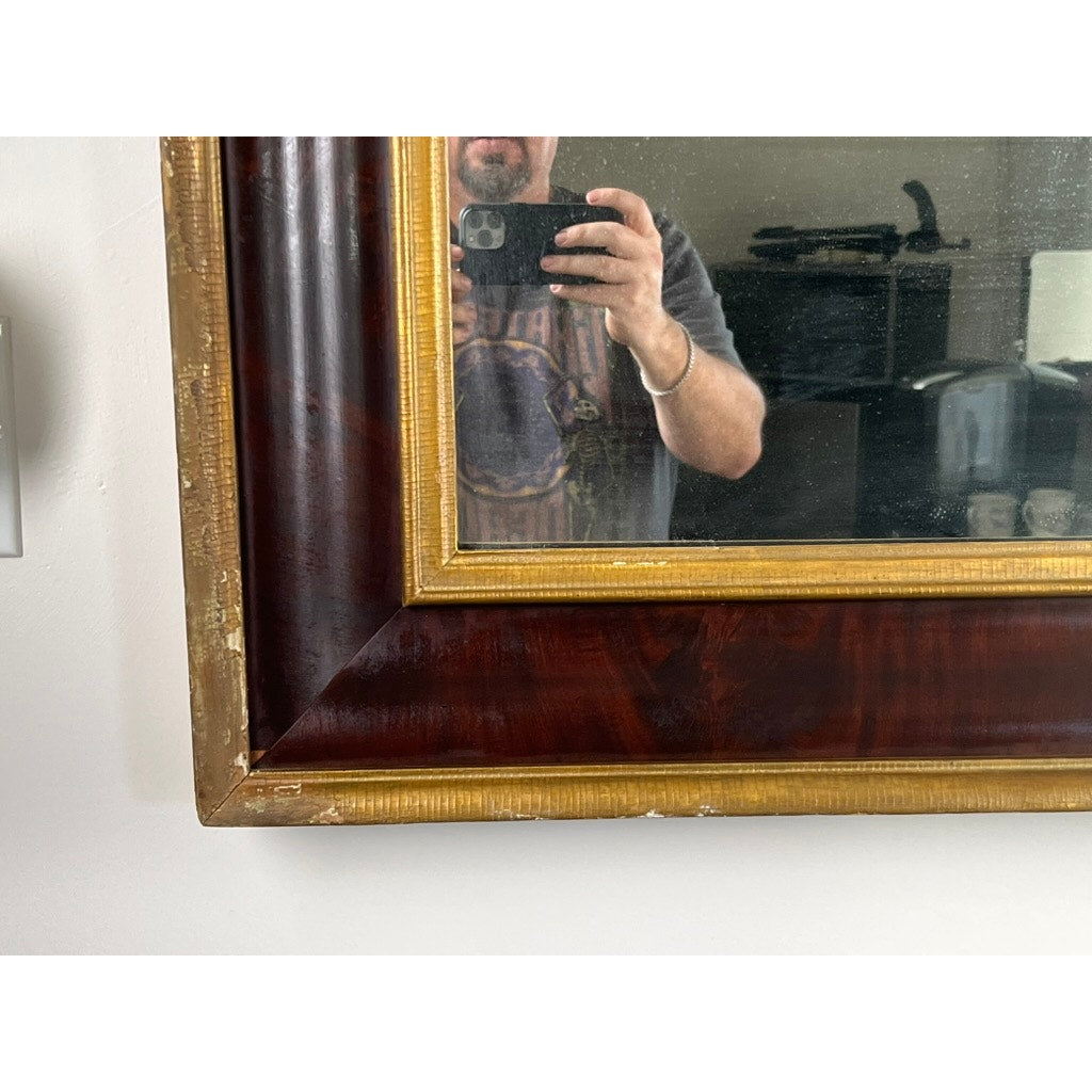 A person snaps a photo of their torso and phone in an Antique American Empire Parcel Gilt Flame Mahogany Ogee Wall Mirror (mid-19th century), with furniture and a lamp visible in the background. Brand: None/Unknown.