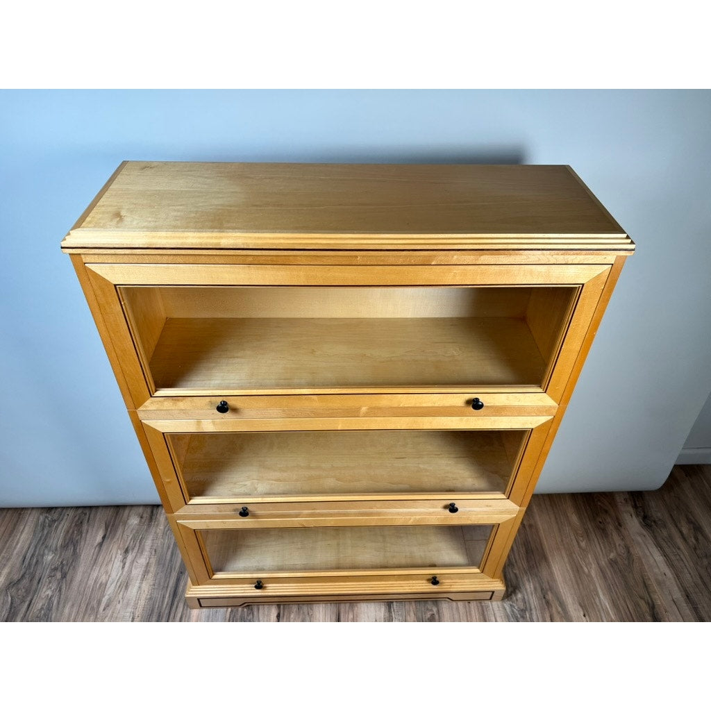 A Vintage Bench Made Maple with Wenge Inlay Three Stack Barrister Bookcase, featuring glass-front doors with black knobs, stands on a wood-patterned floor against a plain light-colored wall.