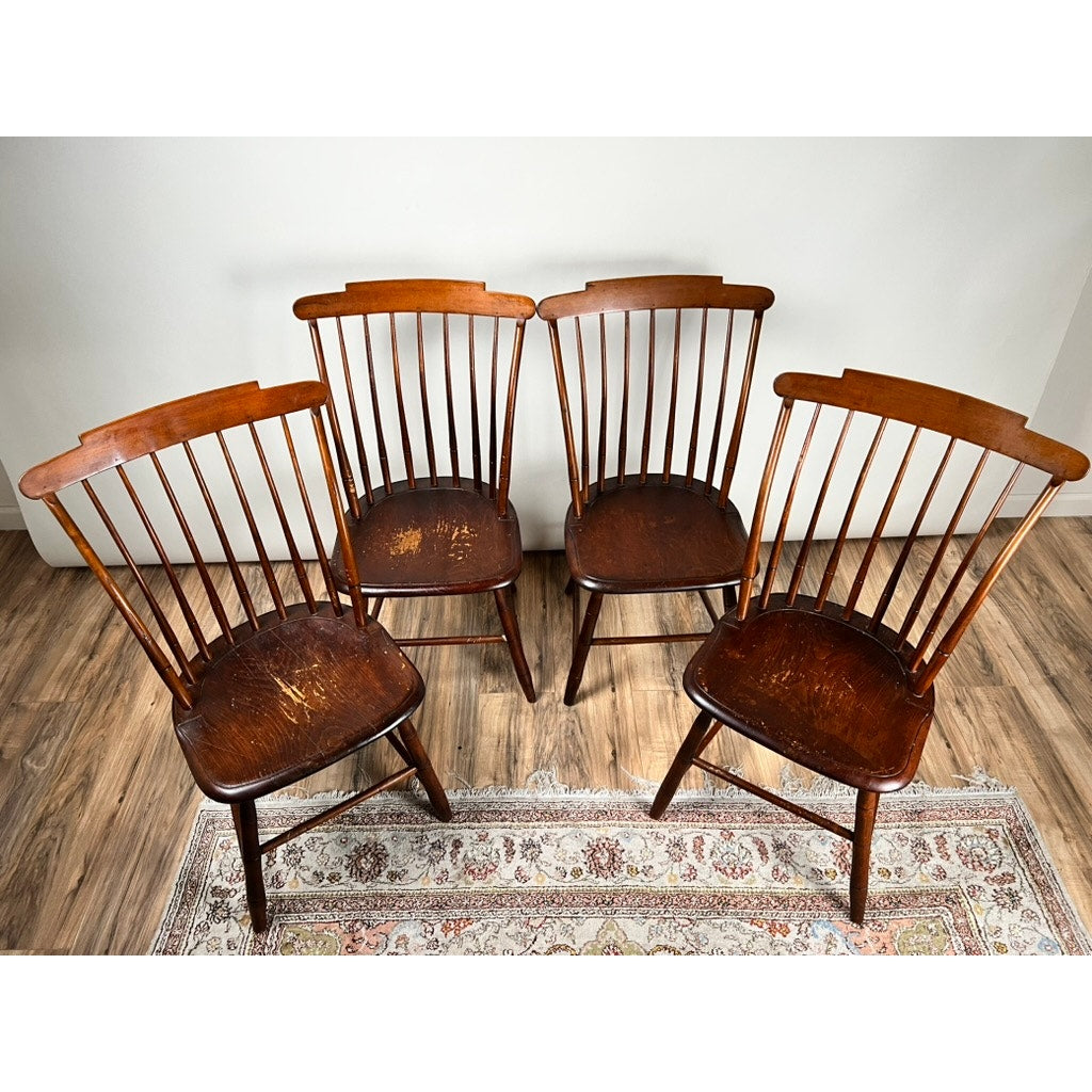 A set of four JR Hunt New Hampshire Step Down Windsor chairs (early 19th c.), signed and featuring rounded backs with vertical slats, is arranged on a patterned rug against a white wall, reflecting classic American style.