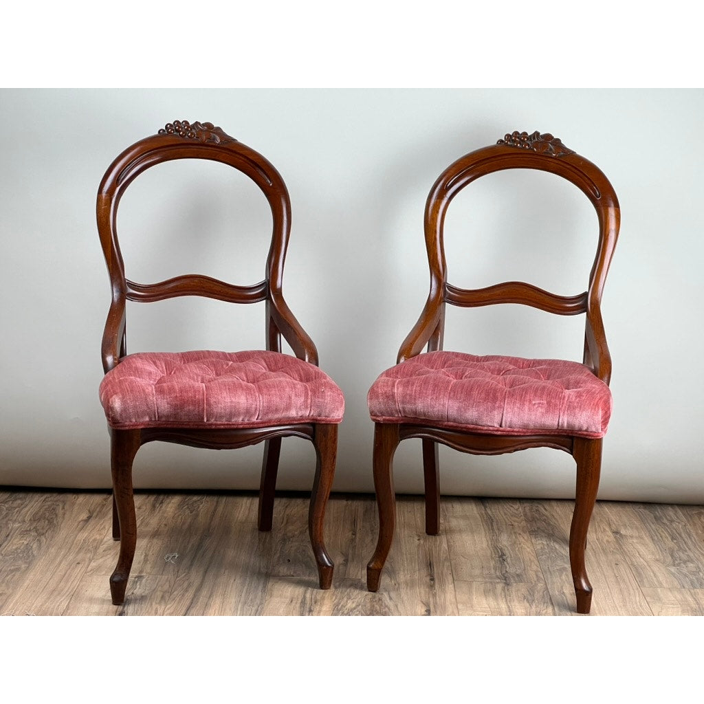 Antique Pair Victorian Walnut Balloon Back Tufted Side Chairs, c. Late 19th Century, featuring ornate carvings and pink velvet tufted seats on walnut frames, displayed against a plain light background on a wooden floor.