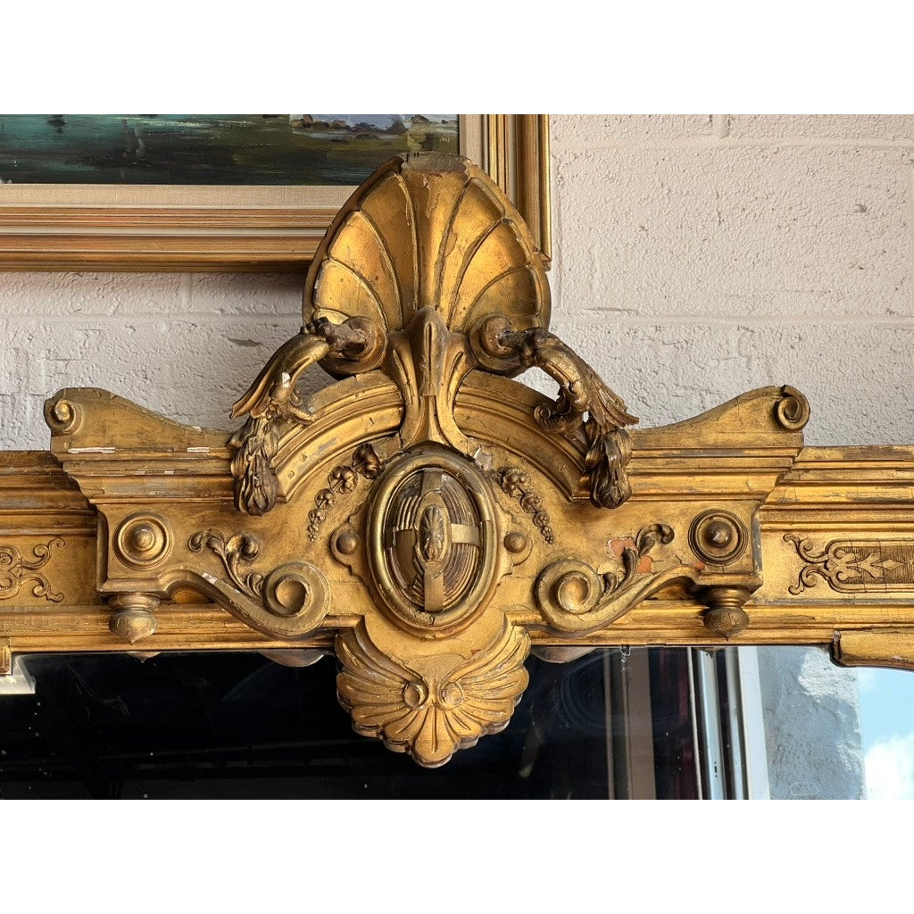 Exceptional Monumental Victorian Renaissance Revival Pier Mirror, circa 1870–1885, featuring an ornate giltwood frame with intricate carvings of two birds facing each other and an oval centerpiece, displayed against a light-colored brick wall.