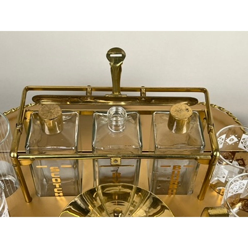 A Vintage Mid Century Modern Bar Caddy c. 1960s displays three glass decanters with gold lettering and cork stoppers, one open, with glasses nearby on the cart’s gleaming surface. Brand: None/Unknown.
