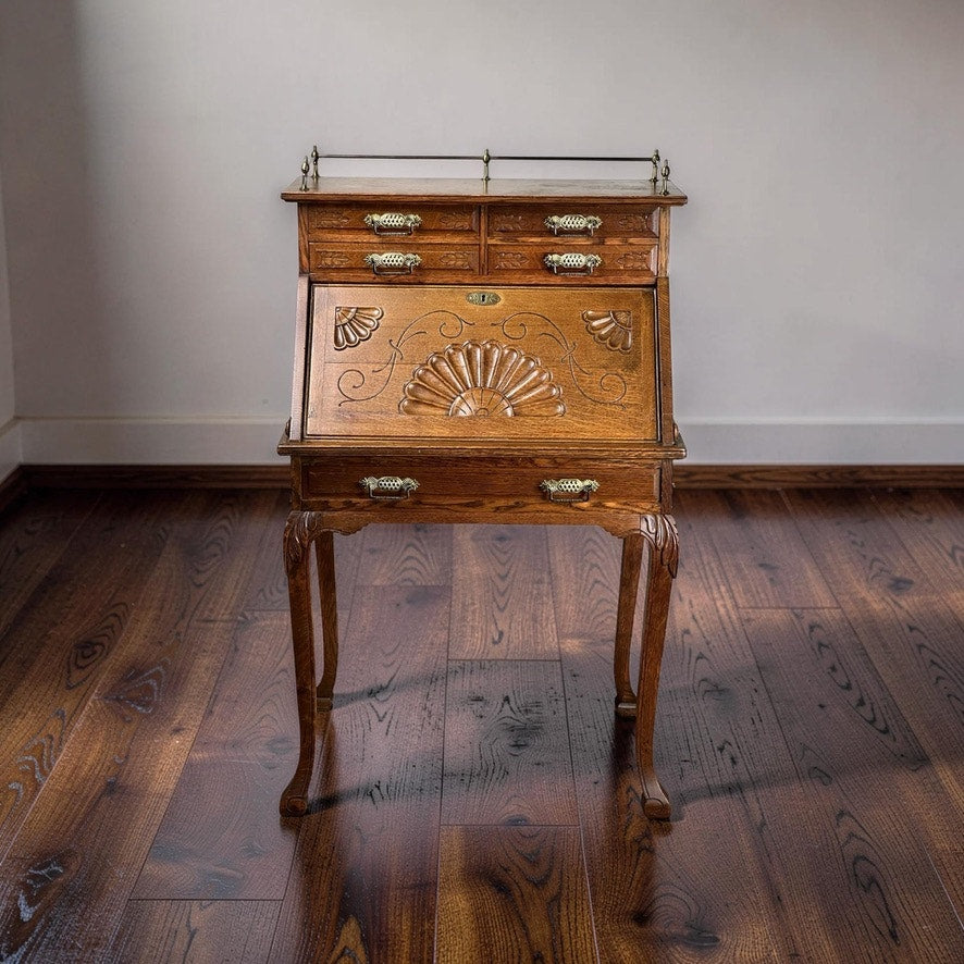 The Antique Victorian Oak Ladies Writing Desk c. 1900 features ornate carving, brass handles, four small drawers, and elegant curved legs—creating a timeless focal point for any room. Brand: Unknown.