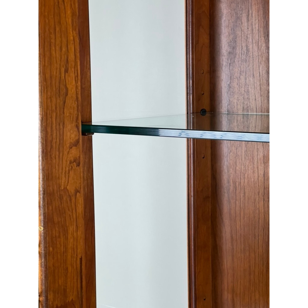 Close-up of the Vintage William IV Style Cherry Glass Door Bookcase by Stickley, featuring a warm cherry finish and a glass shelf between two wood panels, shown against a light-colored wall.
