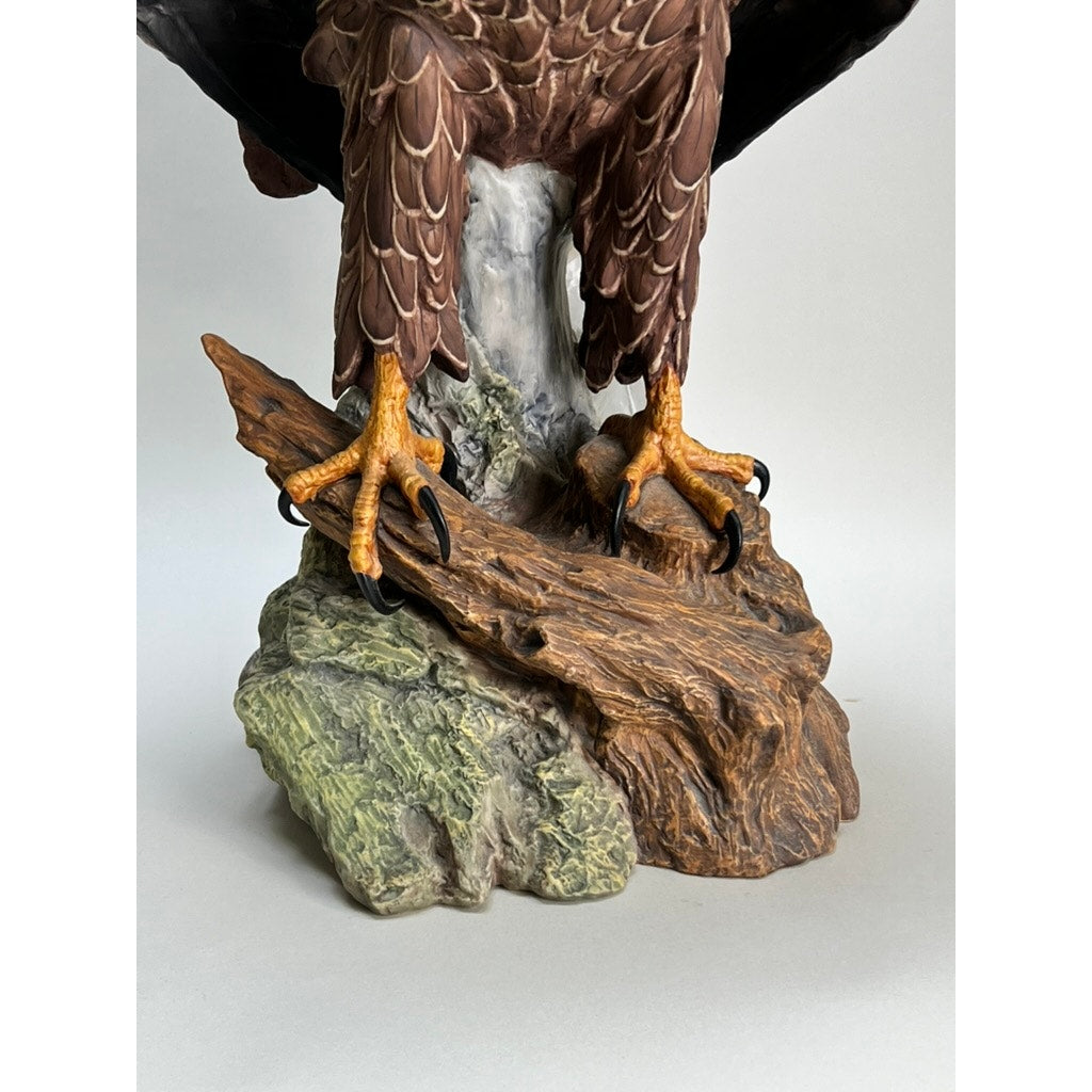A close-up shows the Rare Kaiser Porcelain American Bald Eagle Sculpture, Limited Edition No. 12/200 by Kaiser, W. Germany—yellow talons grip a textured brown rock with part of a grey tree trunk behind, set against a plain light background.